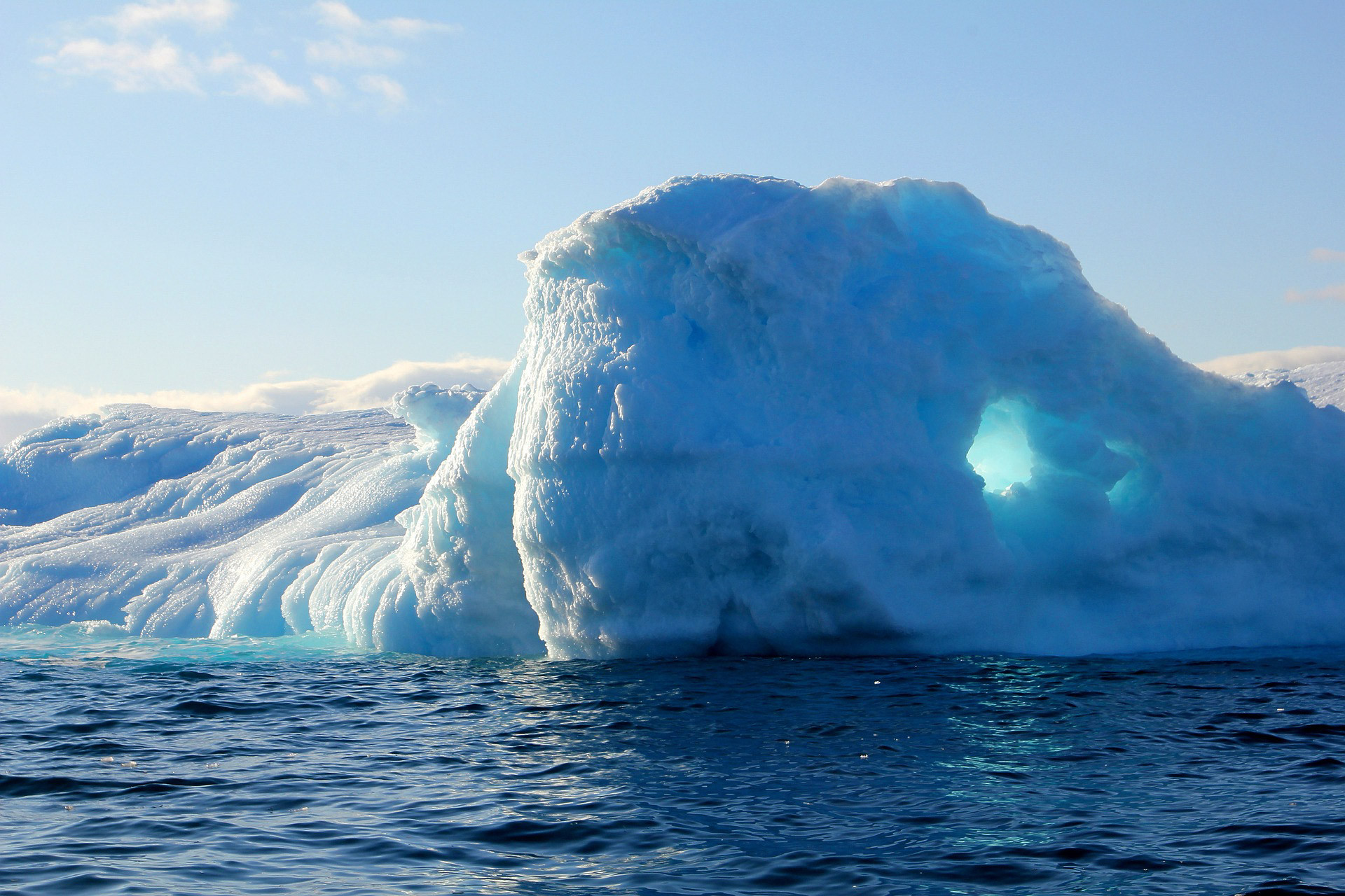 A blue and white iceberg rises out of the water at an icy landscape