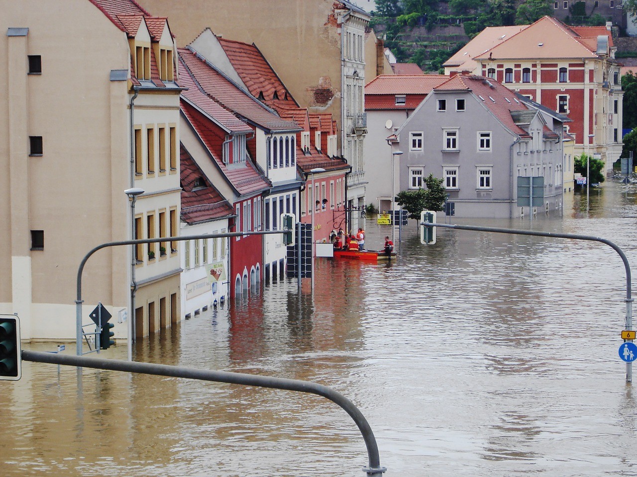 Eine Straße steht komplett unter Wasser, Menschen in einem Schlauchboot retten Personen aus einem Haus