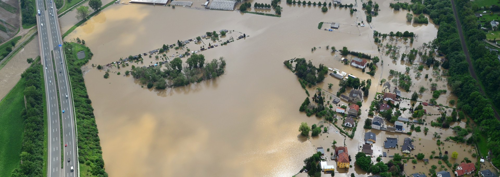 Mit Hochwasser überfluteter Landschaftszug. Häuser und Straßen stehen unter Wasser.