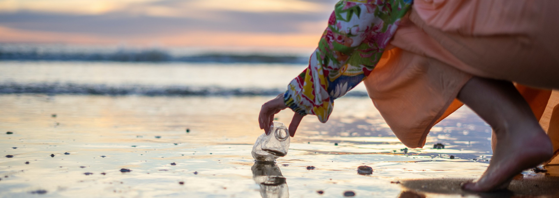 Eine Person hebt eine Plastikflasche von einem Strand auf