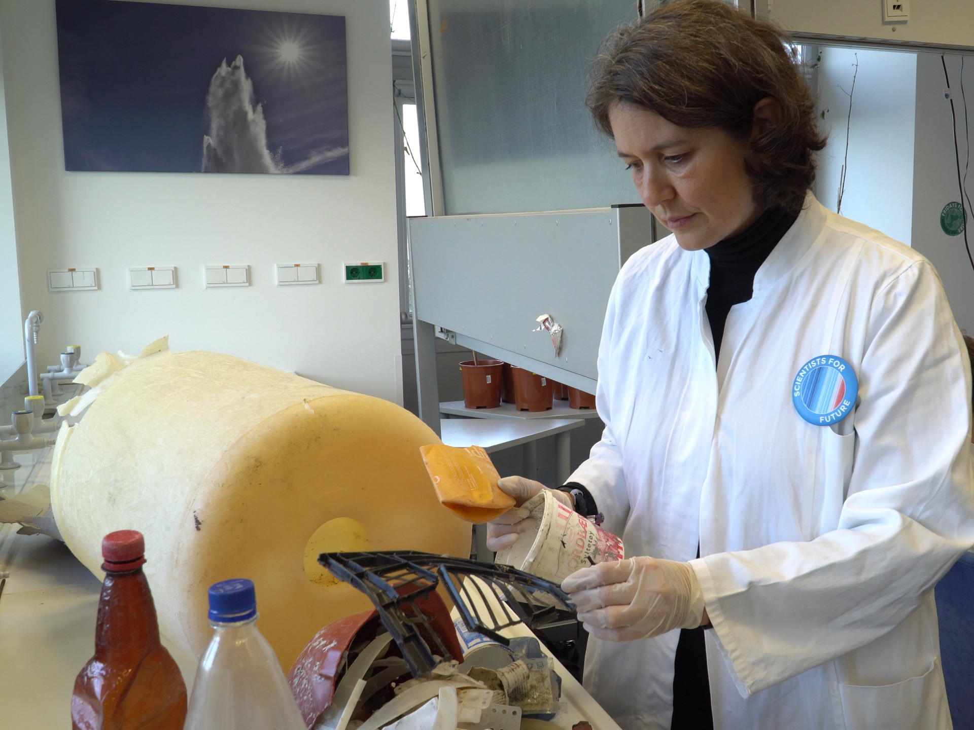 Scientist in white lab coat with a big yellow bucket turned marine litter
