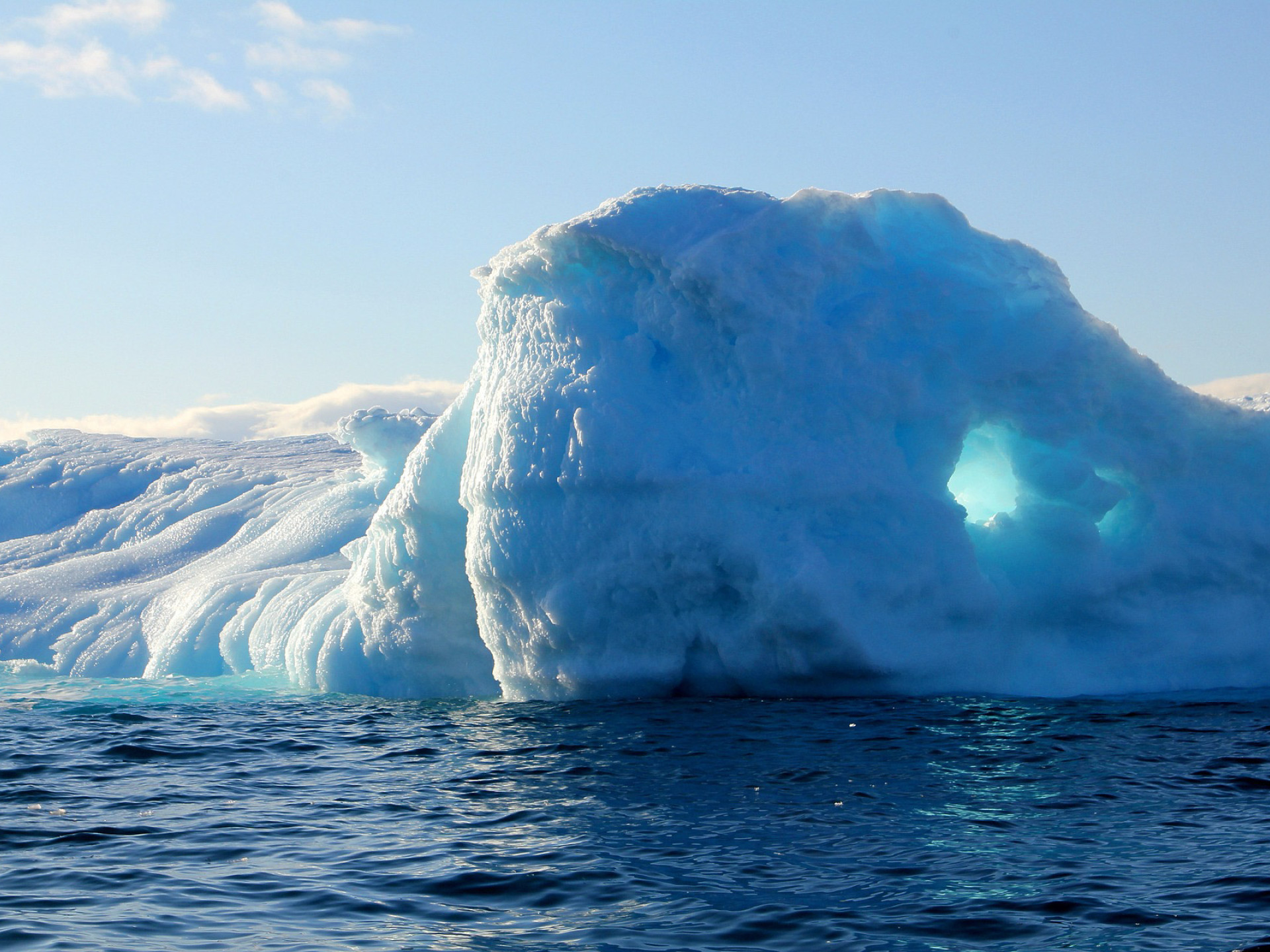 Ein blau-weißer Eisberg ragt an einer Eislandschaft aus dem Wasser