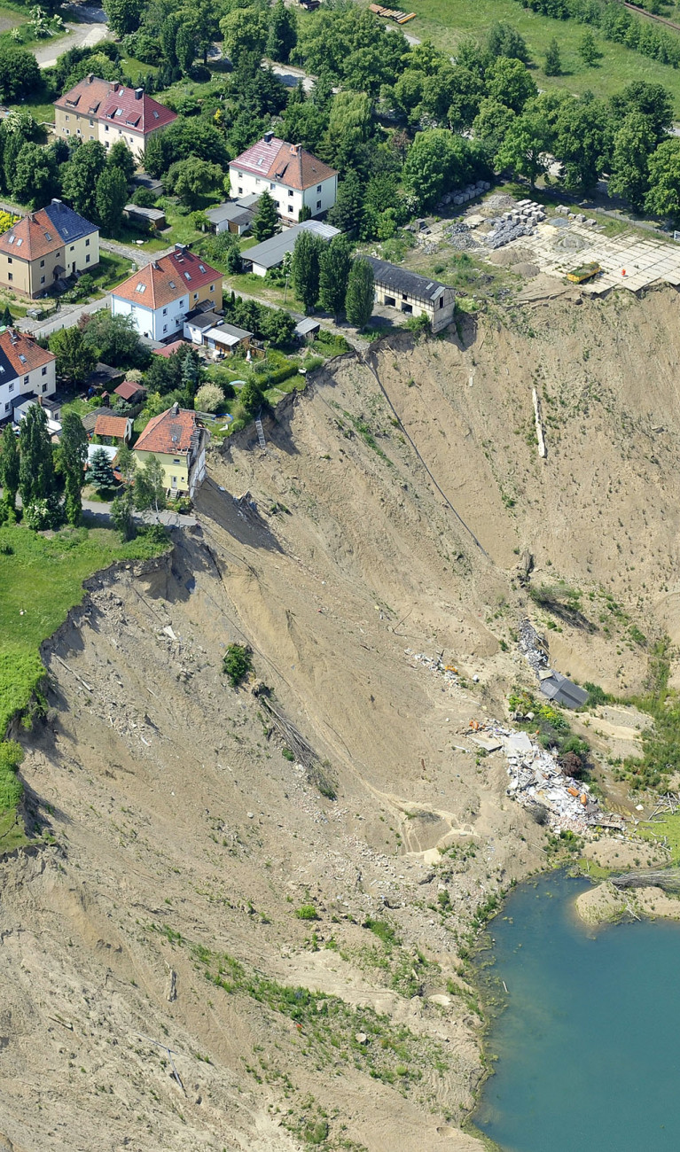 Houses near a collapsed hill with no vegetation, leading down to a small lake.