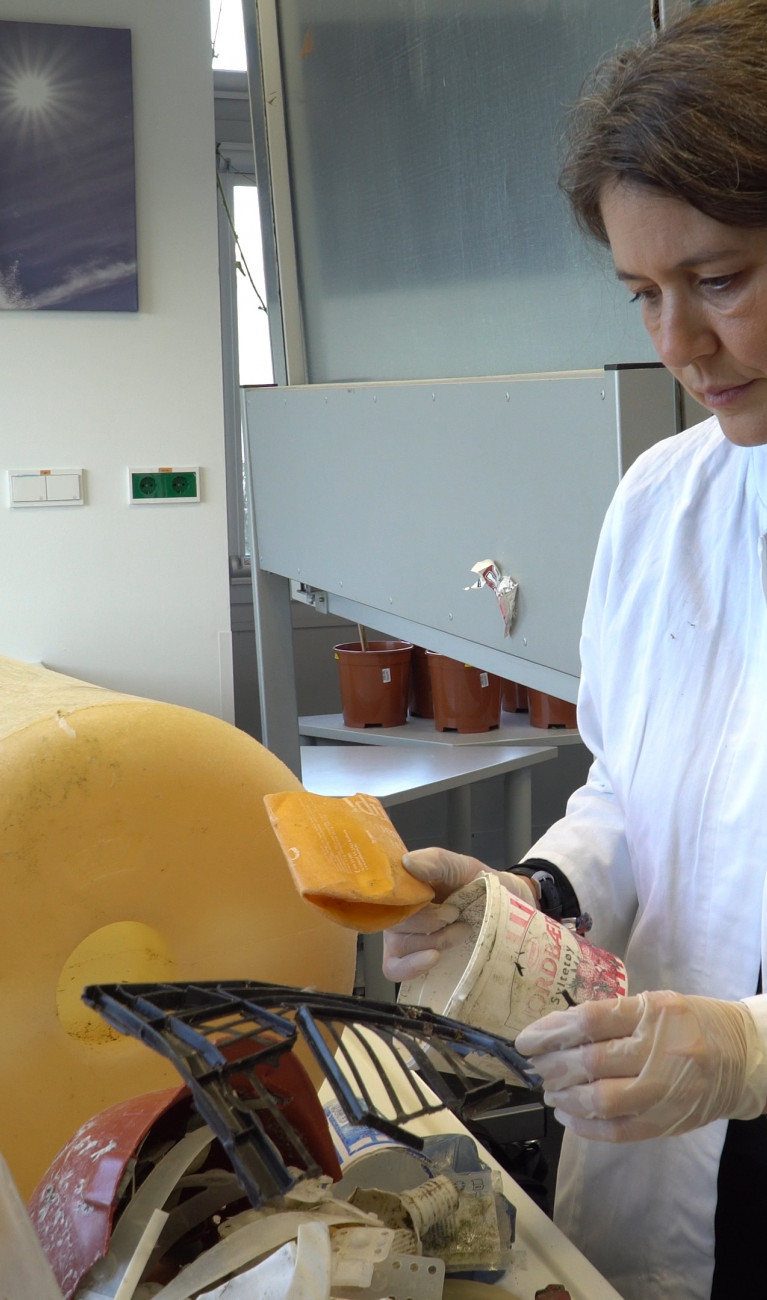 Scientist in white lab coat with a big yellow bucket turned marine litter