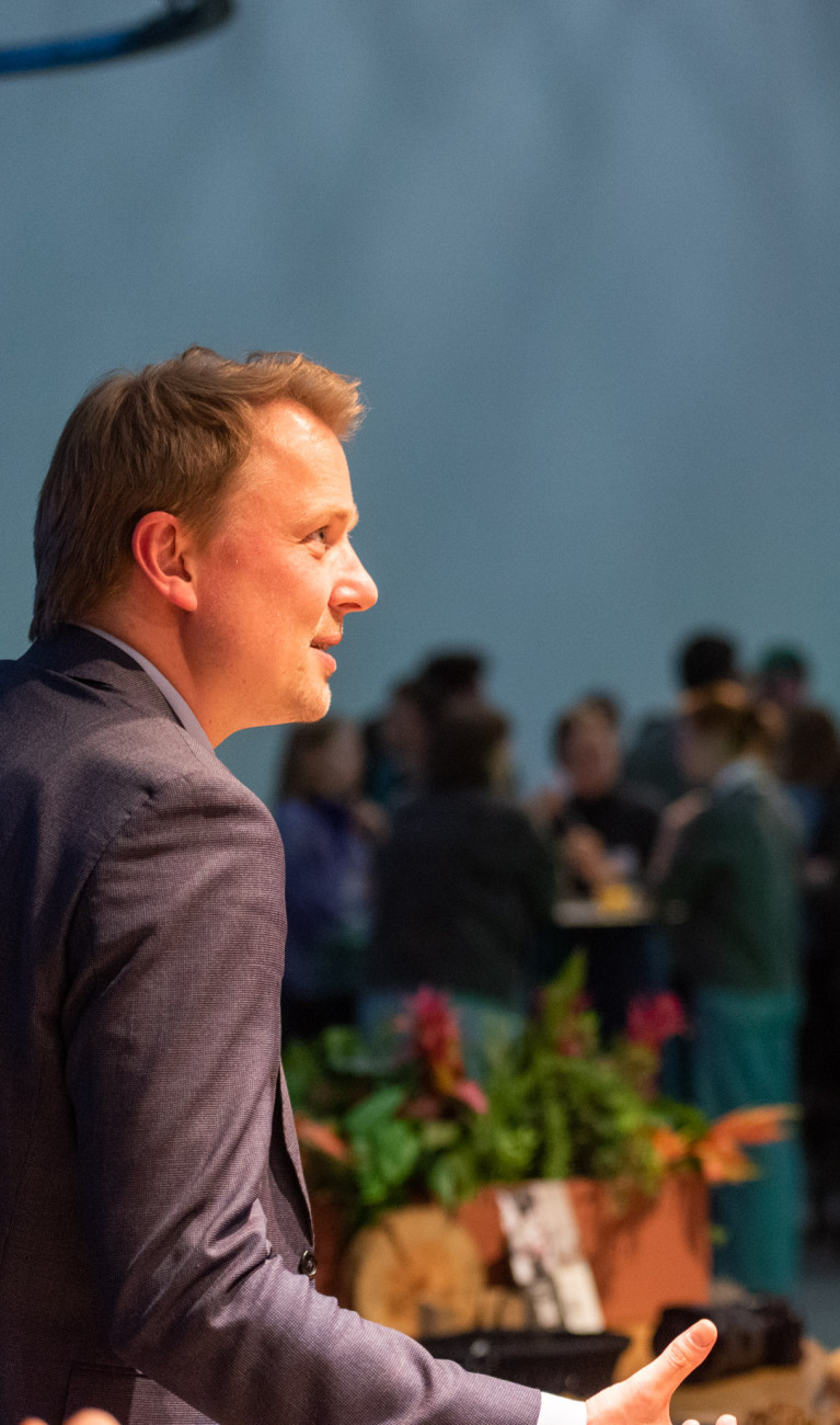 Zwei Männer unterhalten sich, im Hintergrund eine Menschenmenge.