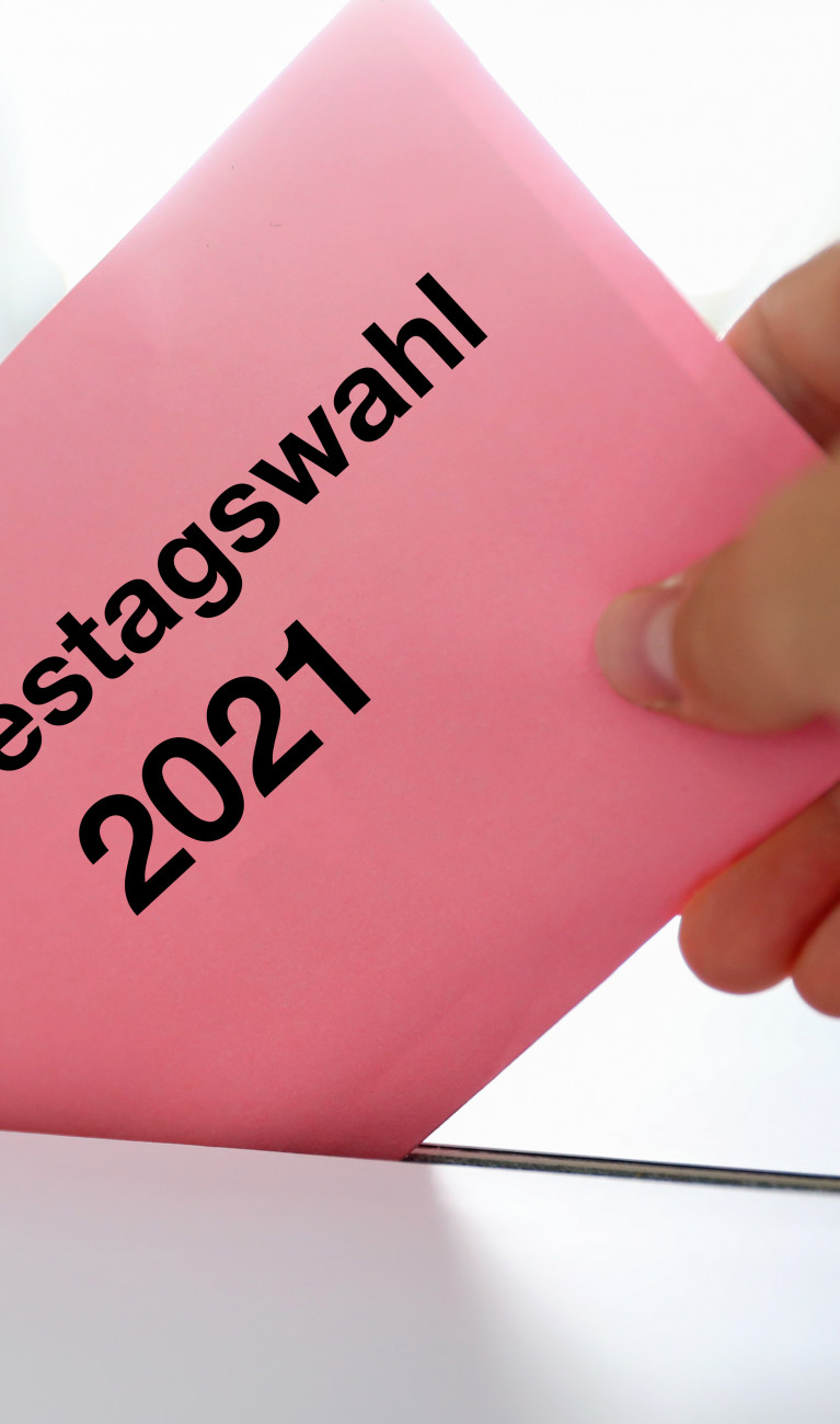 Hand wirft Umschlag mit Aufschrift "Bundestagswahl 2021" in Wahlurne