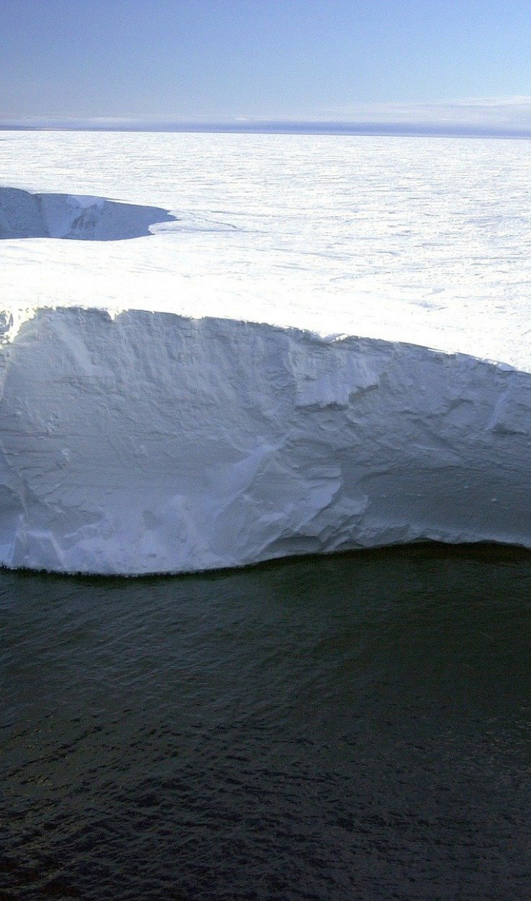 Ein große weiße Eisfläche ragt aus dem dunklen Meer