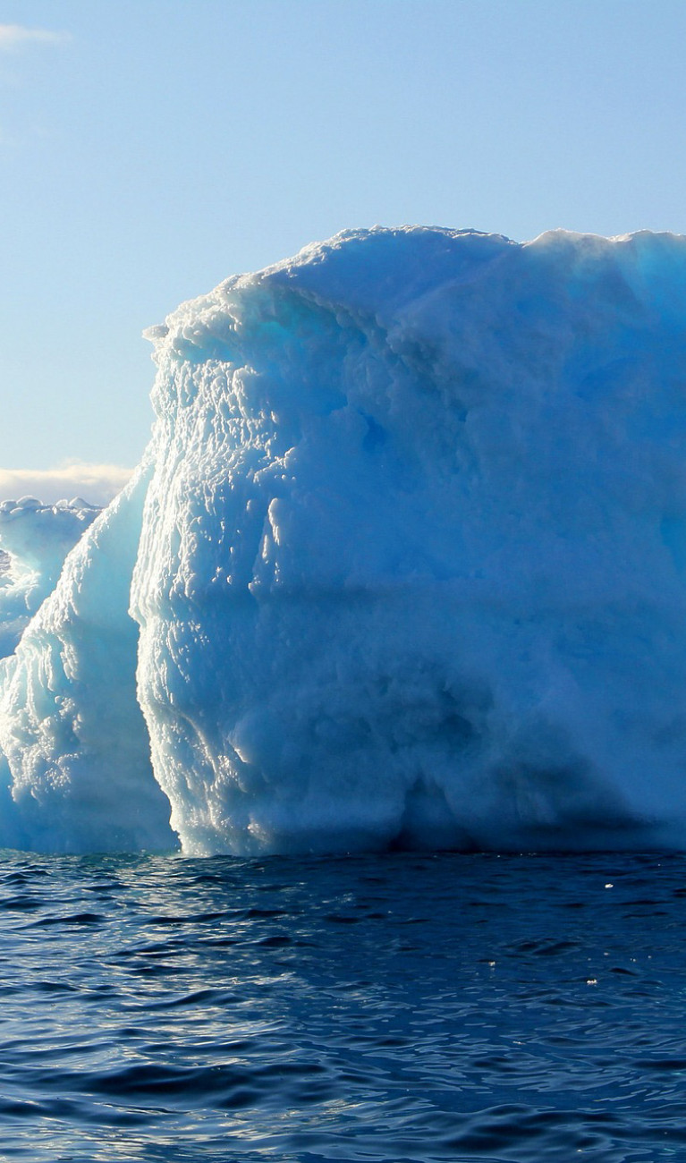 A blue and white iceberg rises out of the water at an icy landscape