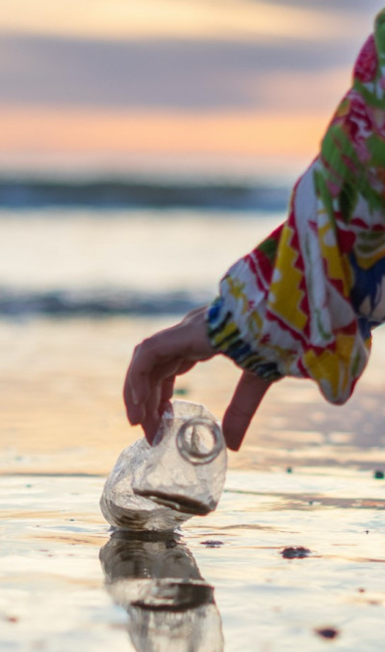 Eine Person hebt eine Plastikflasche von einem Strand auf