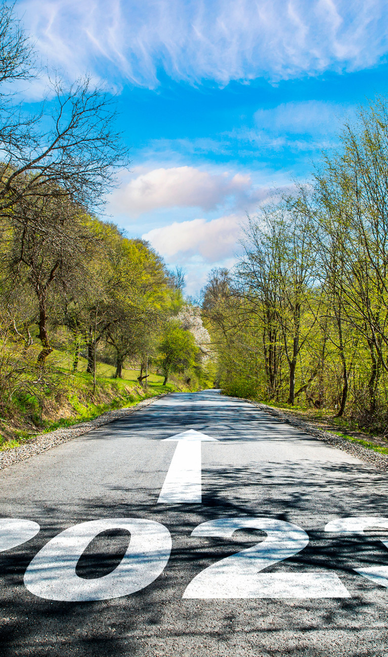 Eine Straße durch grüne Landschaft, auf der Fahrbahn steht groß "2023" - ein Pfeil zeigt darüber geradeaus die Straße hinauf.