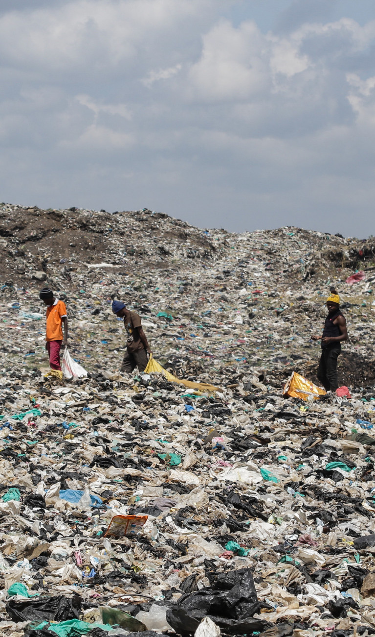 Drei Personen laufen über eine riesige Müllhalde mit Plastik und anderem Müll