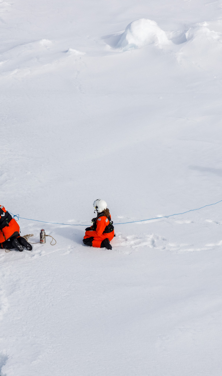 Wissenschaftler:innen fischen ein Müllteil vor einer Eisscholle aus dem Wasser