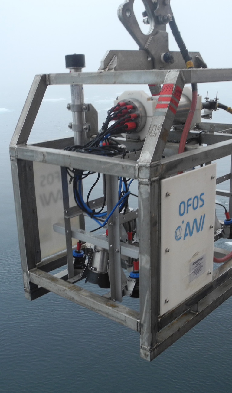 Scientific instruments in a metal cage above the ocean with scattered pieces of ice floating on it