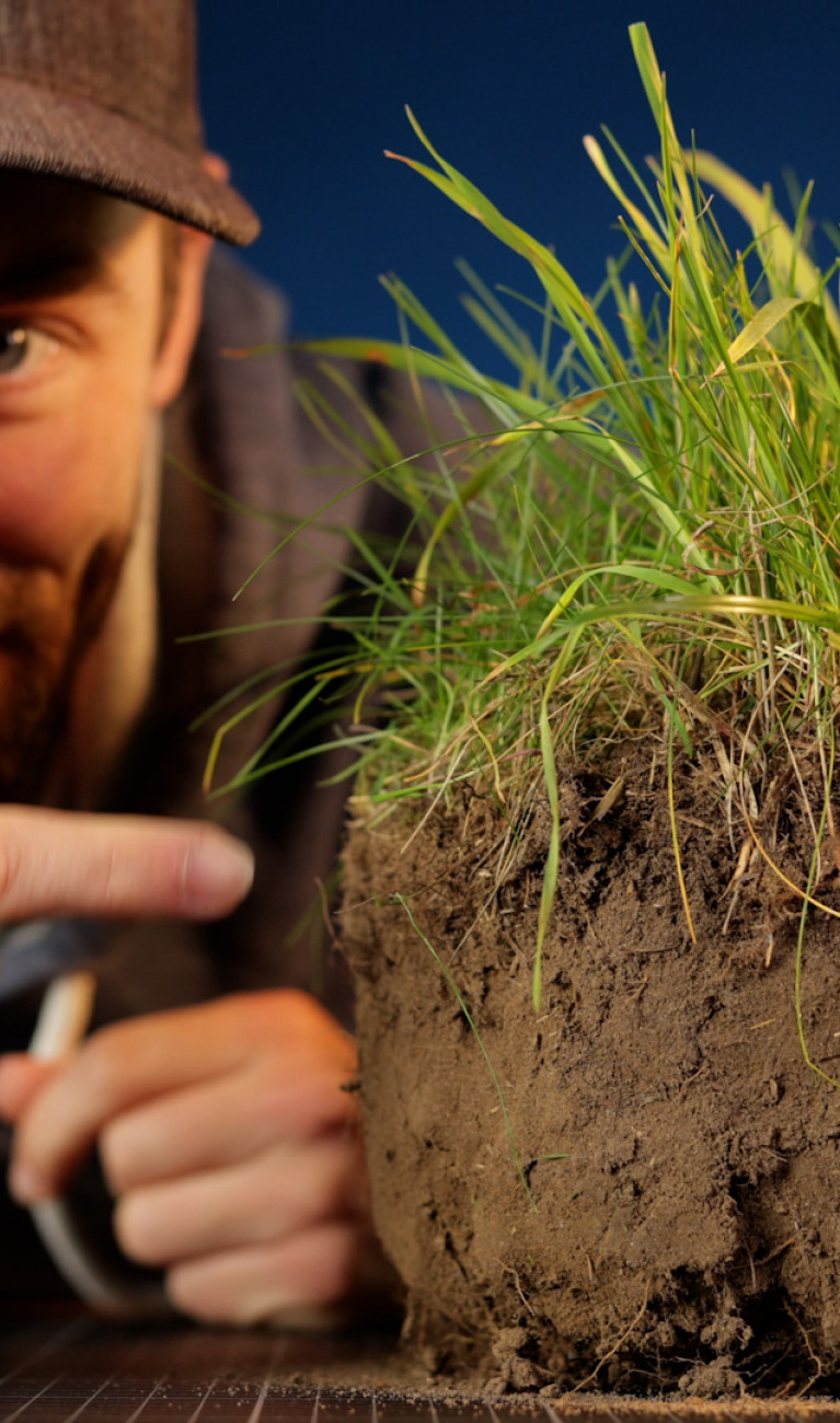 Standbild aus dem Film: Unser YouTuber mit einem ausgestochenen Stück Boden, wo oben das Gras rauswächst.