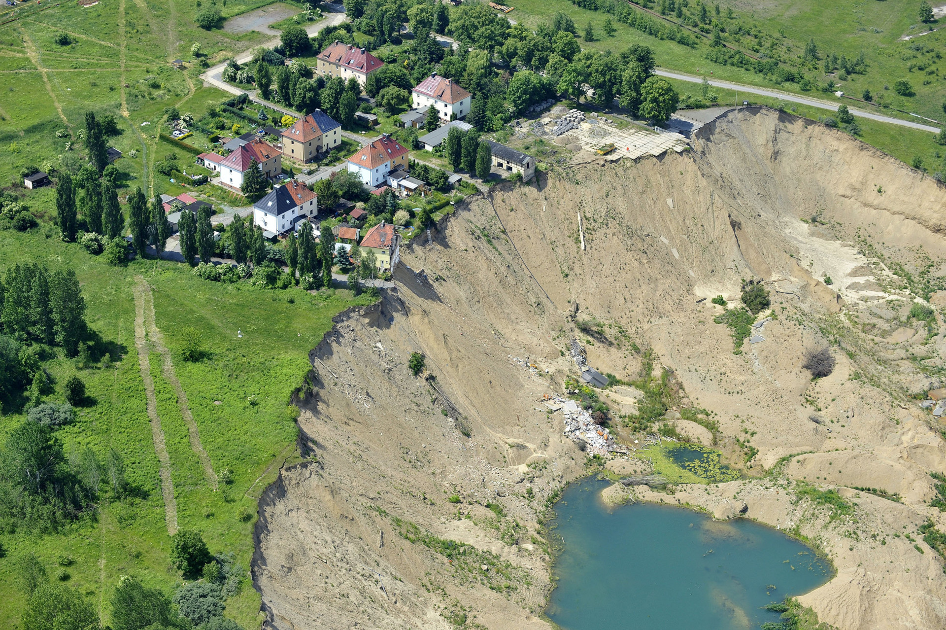Houses near a collapsed hill with no vegetation, leading down to a small lake.