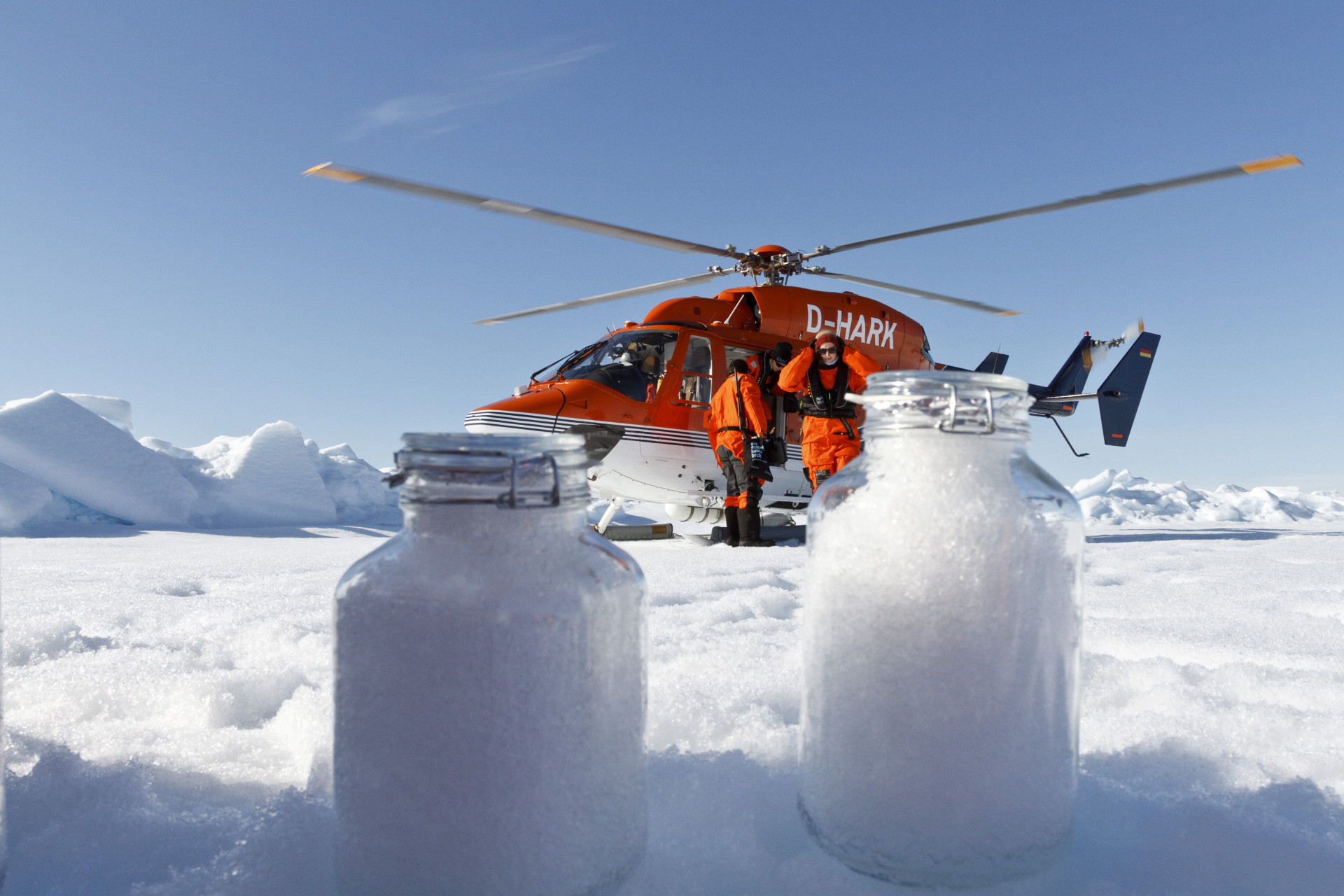 Samples of snow in mason jars with a red helicopter in the background