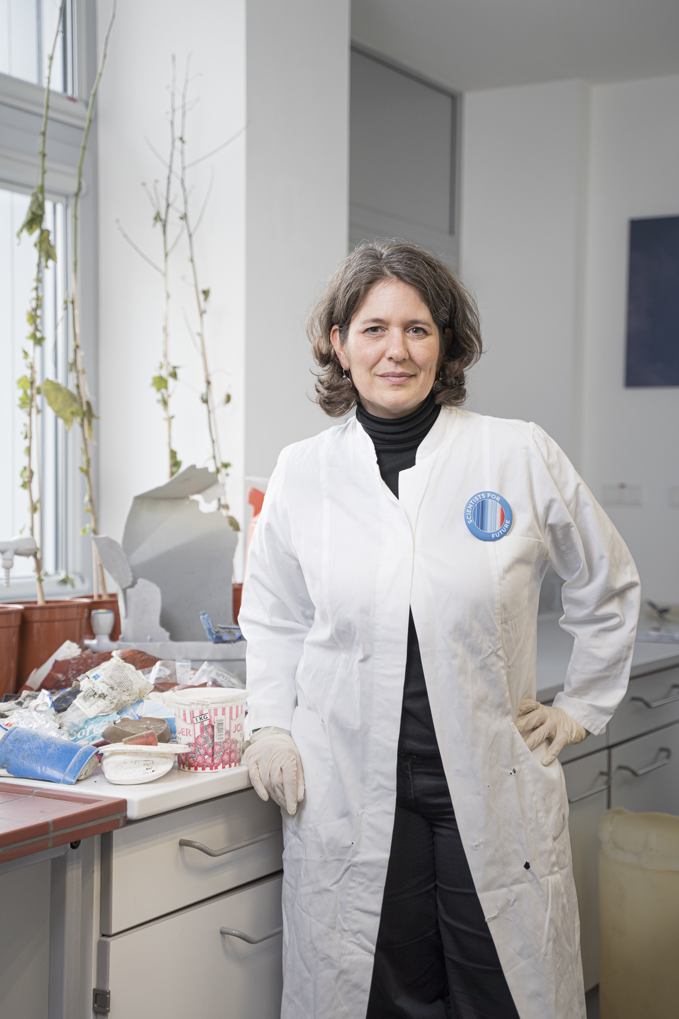 Scientist Melanie Bergmann in a white lab coat in front of a collection of plastic waste