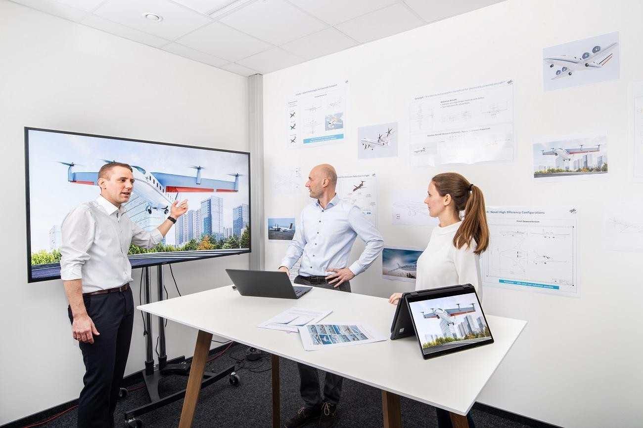 Three scientists in front of monitors and laptops discussing aircraft concepts.