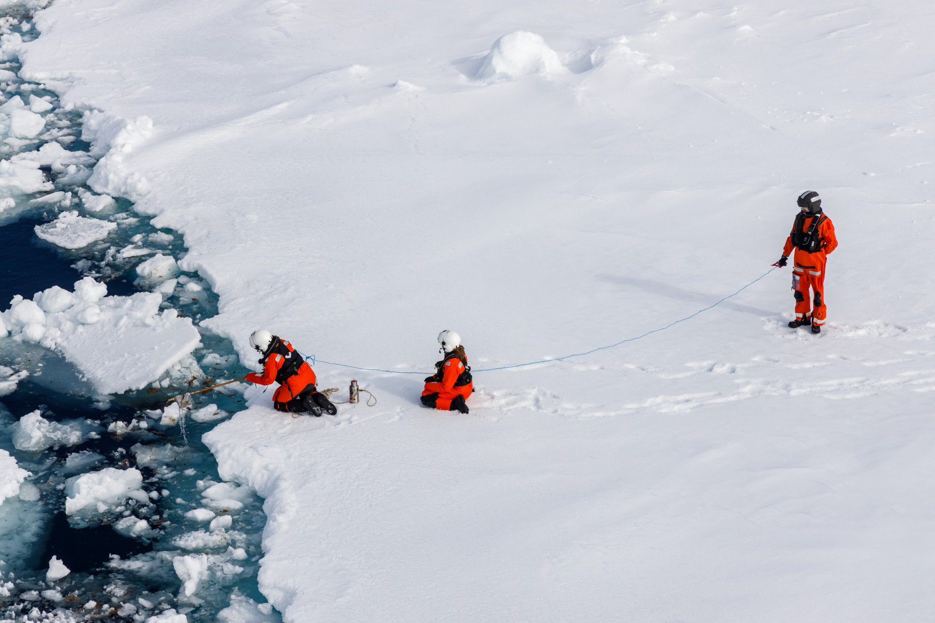 Scientists on an ice floe, fishing a piece of trash out of the water