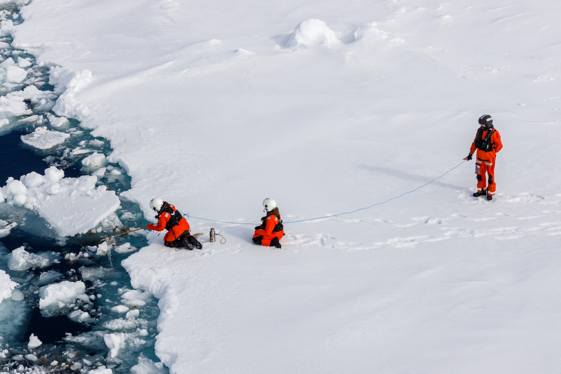 Wissenschaftler:innen fischen ein Müllteil vor einer Eisscholle aus dem Wasser