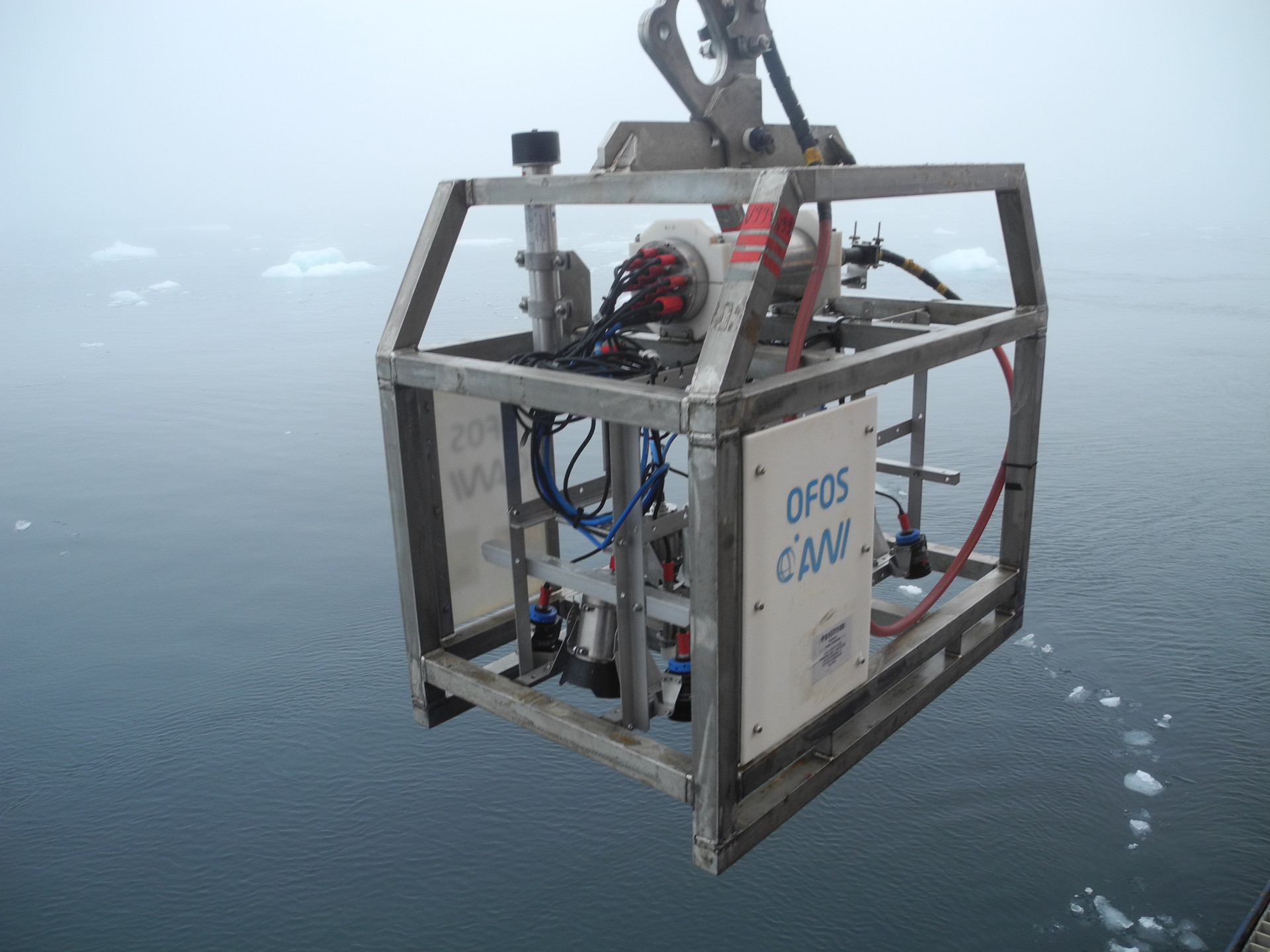 Scientific instruments in a metal cage above the ocean with scattered pieces of ice floating on it