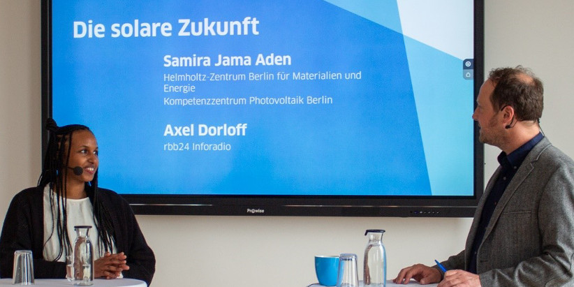 Samira Jama Aden steht an einem Stehtisch und spricht im Podcast über bauwerkintegrierte Photovoltaik