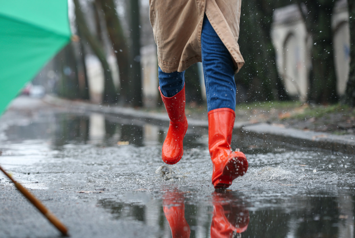 Eine Frau mit roten Gummistiefeln geht durch den Regen.