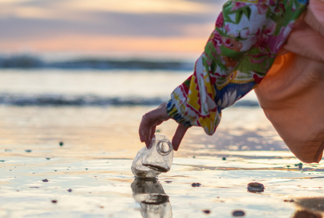 Eine Person hebt eine Plastikflasche von einem Strand auf