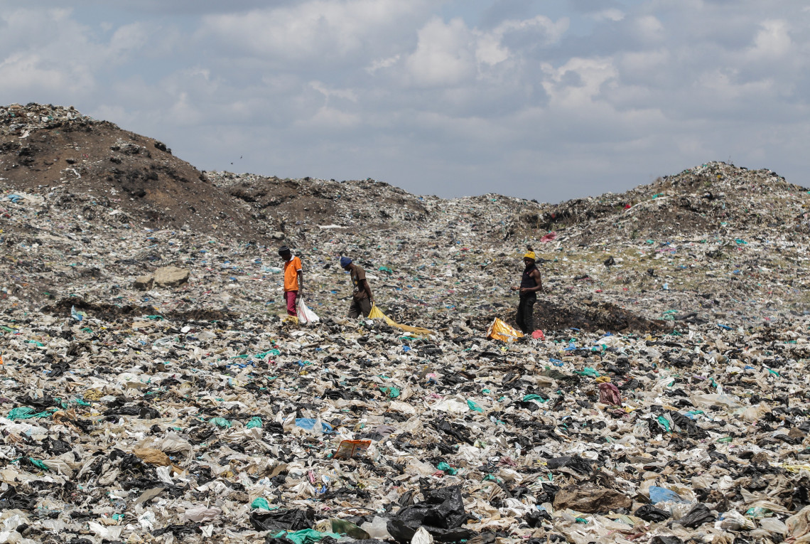 Drei Personen laufen über eine riesige Müllhalde mit Plastik und anderem Müll