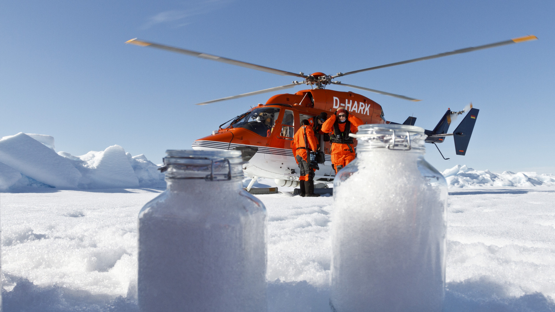 Einweckgläser mit Schneeproben vor rotem Hubschrauber in der Arktis