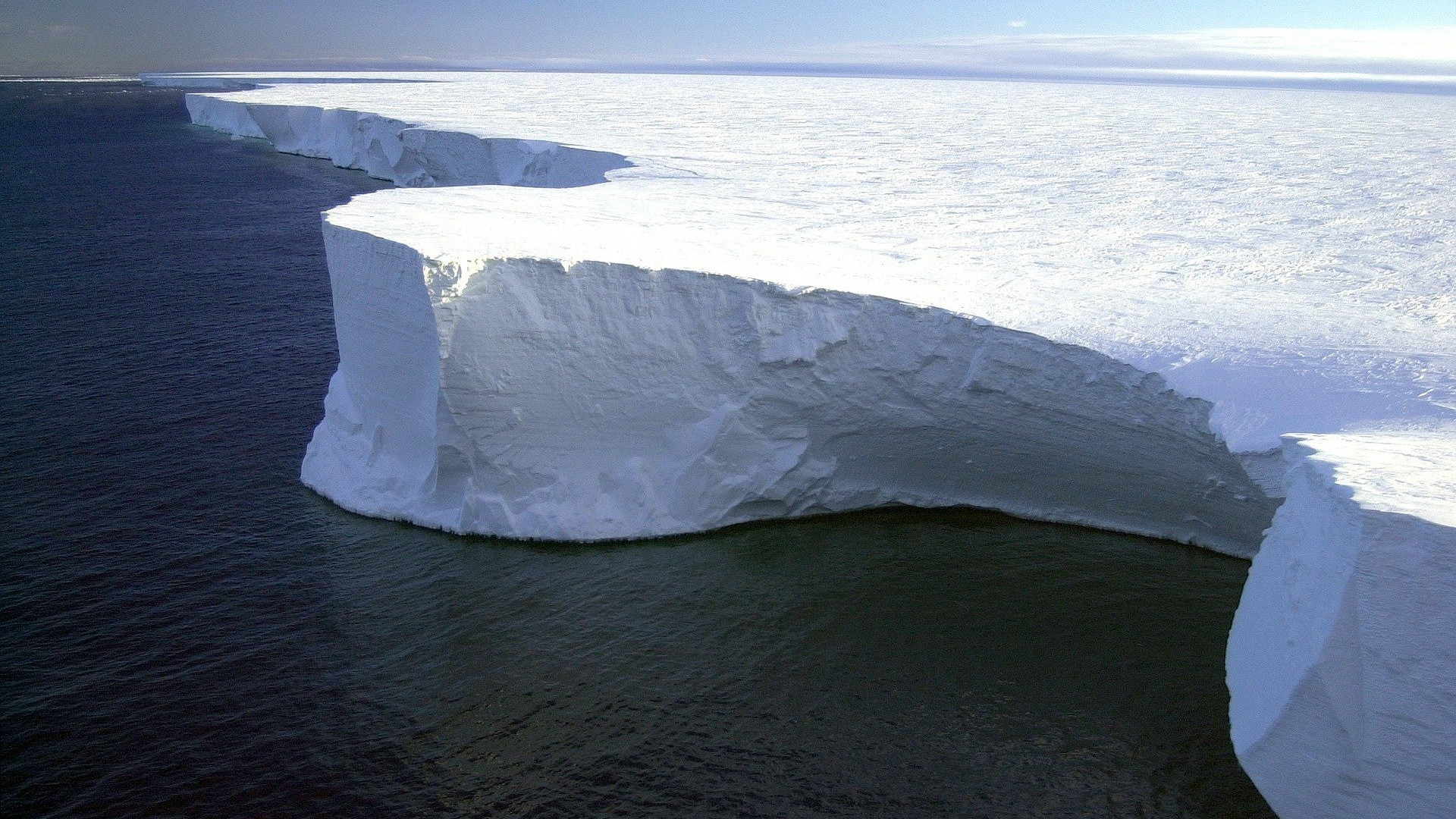Ein große weiße Eisfläche ragt aus dem dunklen Meer