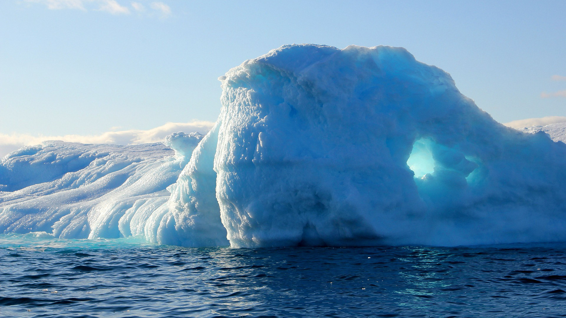 Ein blau-weißer Eisberg ragt an einer Eislandschaft aus dem Wasser