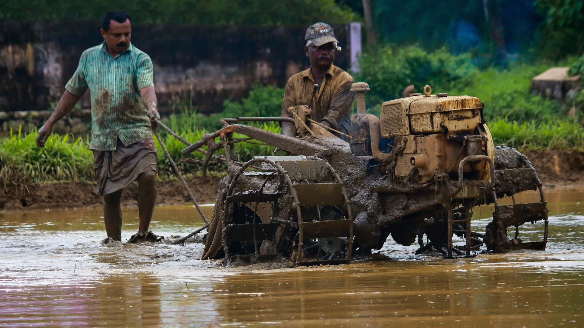 Zwei Männer mit Traktor waten durch ein überschwemmtes Gebiet