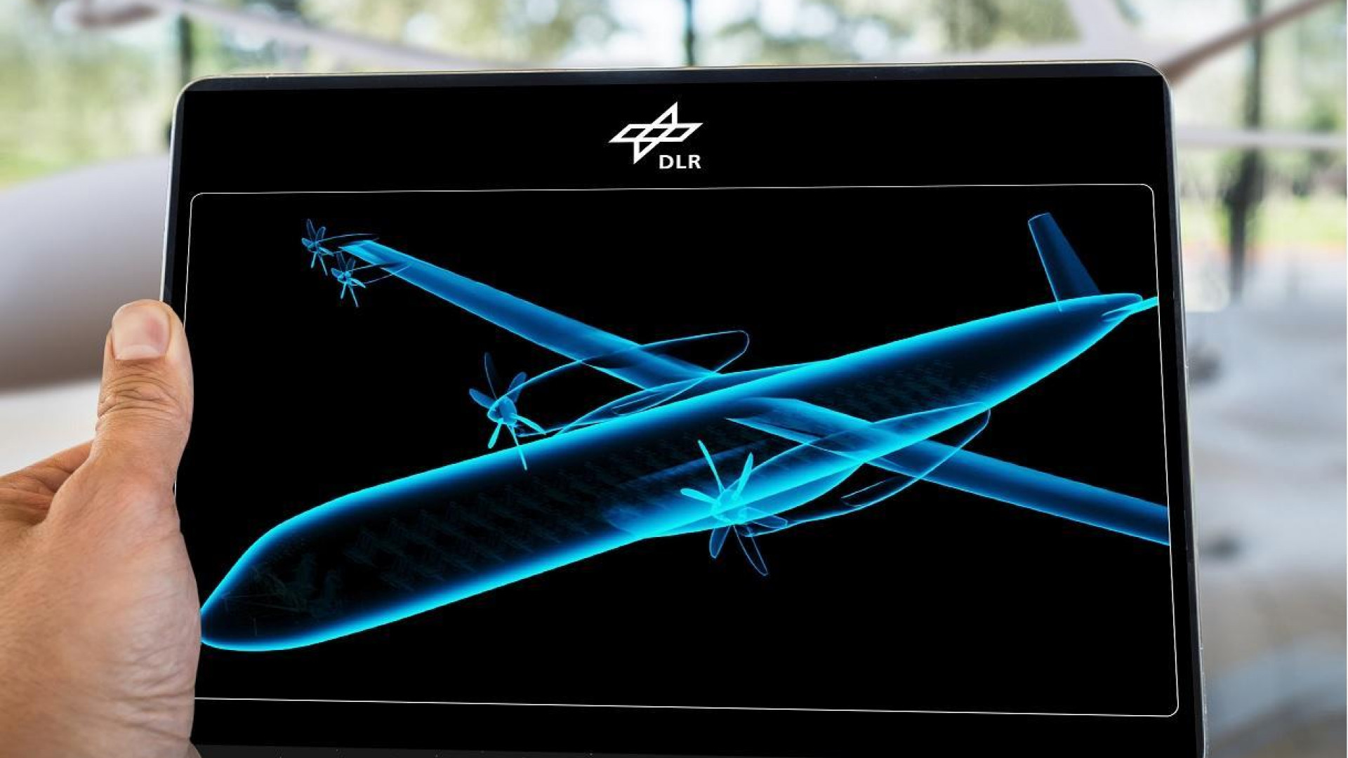 Eine futuristische Silhouette eines Flugzeugs auf einem Tablet, den jemand in der Hand hält.