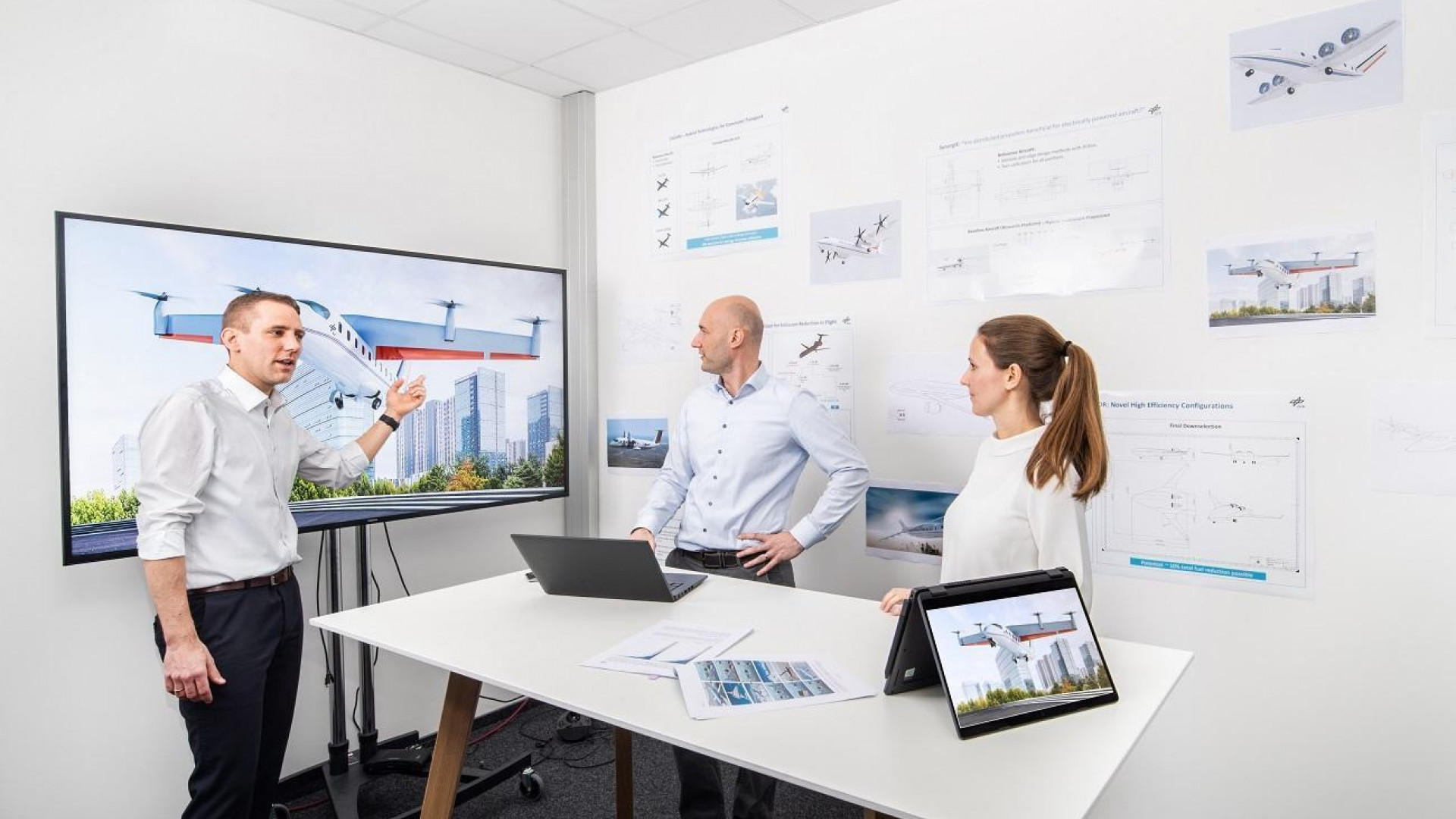 Three scientists in front of monitors and laptops discussing aircraft concepts.