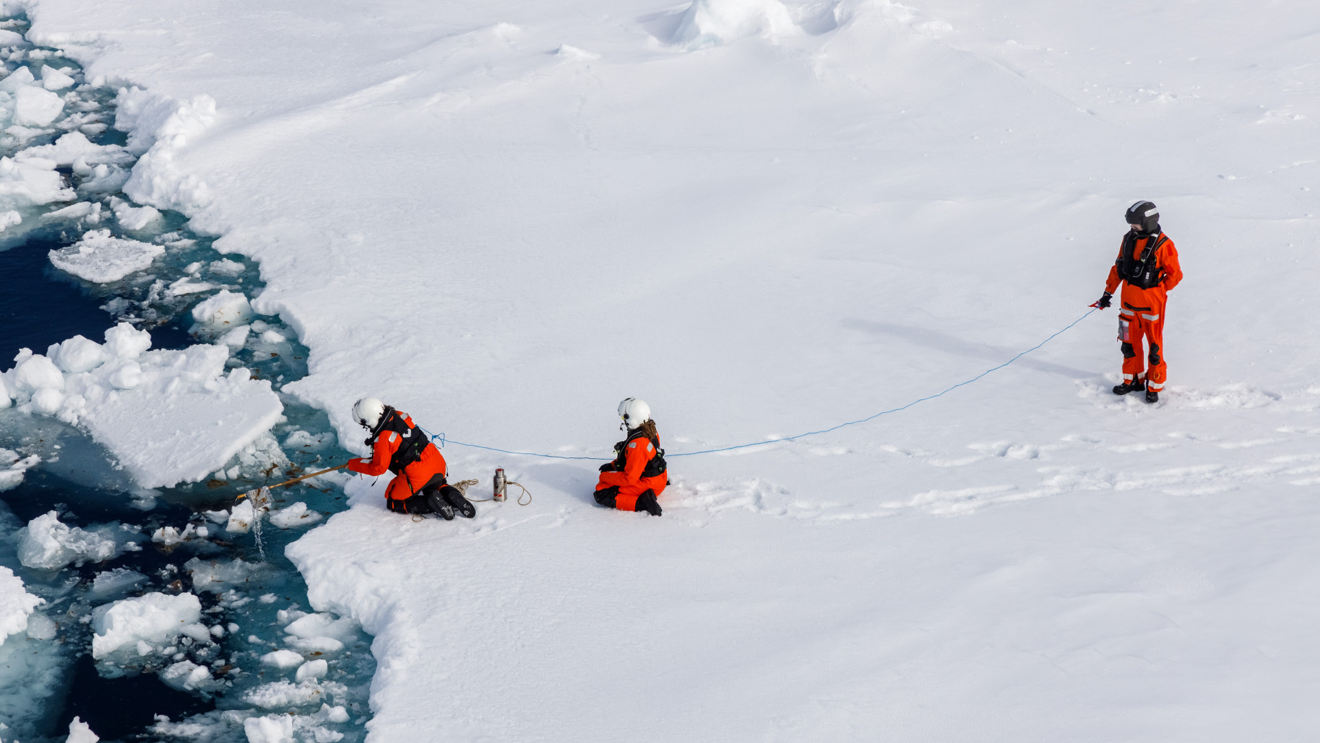 Wissenschaftler:innen fischen ein Müllteil vor einer Eisscholle aus dem Wasser