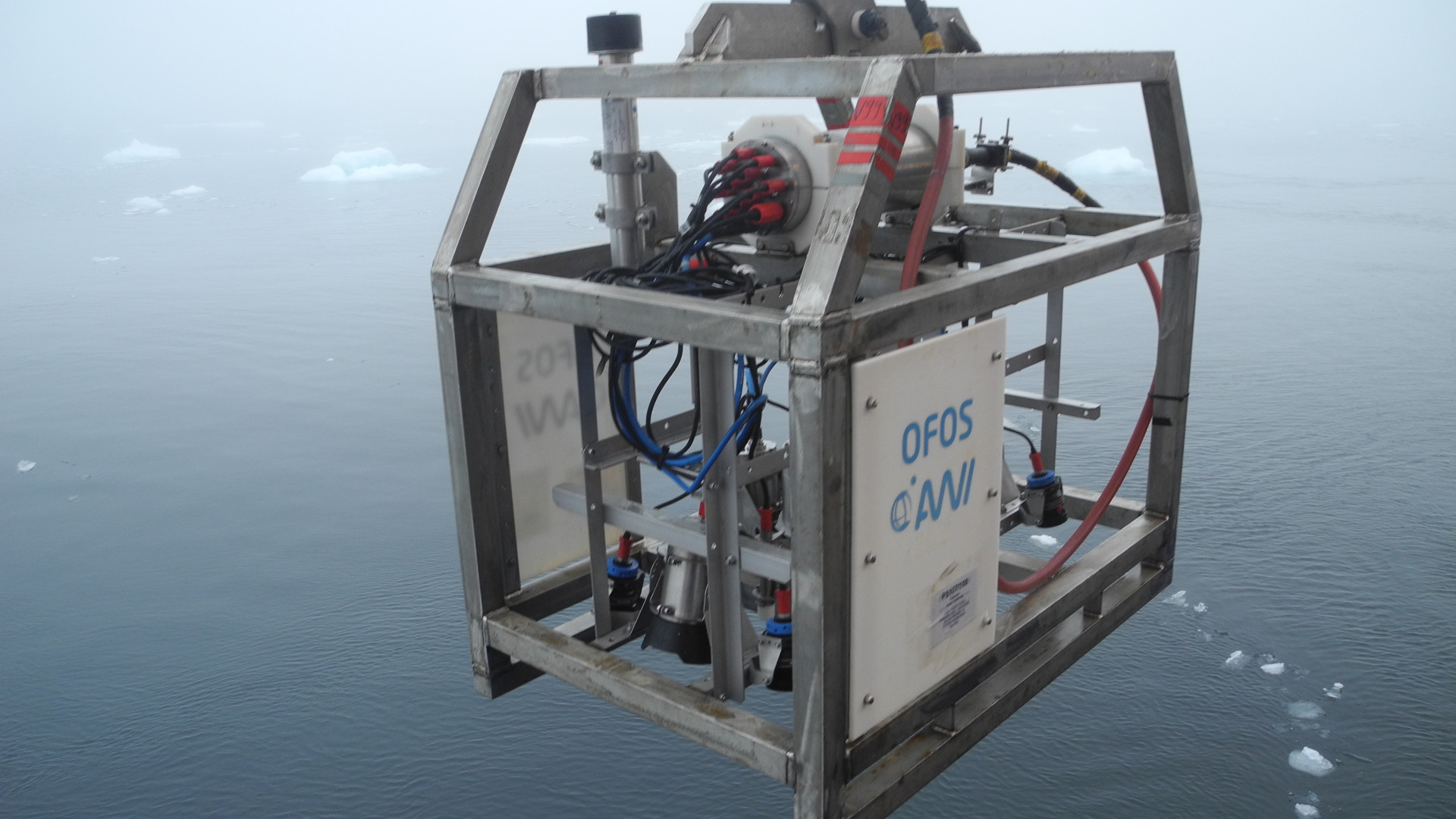 Scientific instruments in a metal cage above the ocean with scattered pieces of ice floating on it
